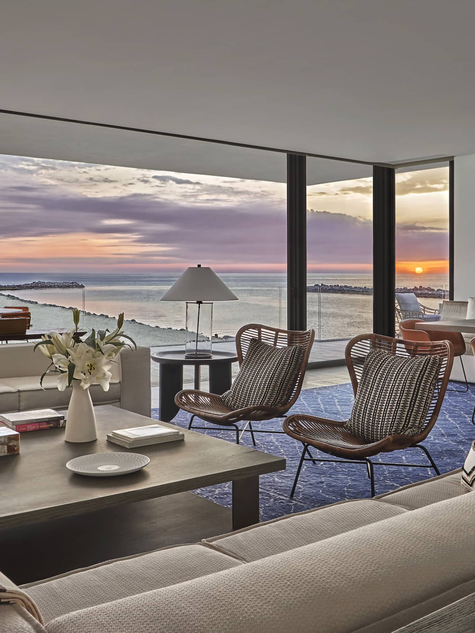 Hotel suite's living and dining area with sunrise view over ocean, through large sliding doors