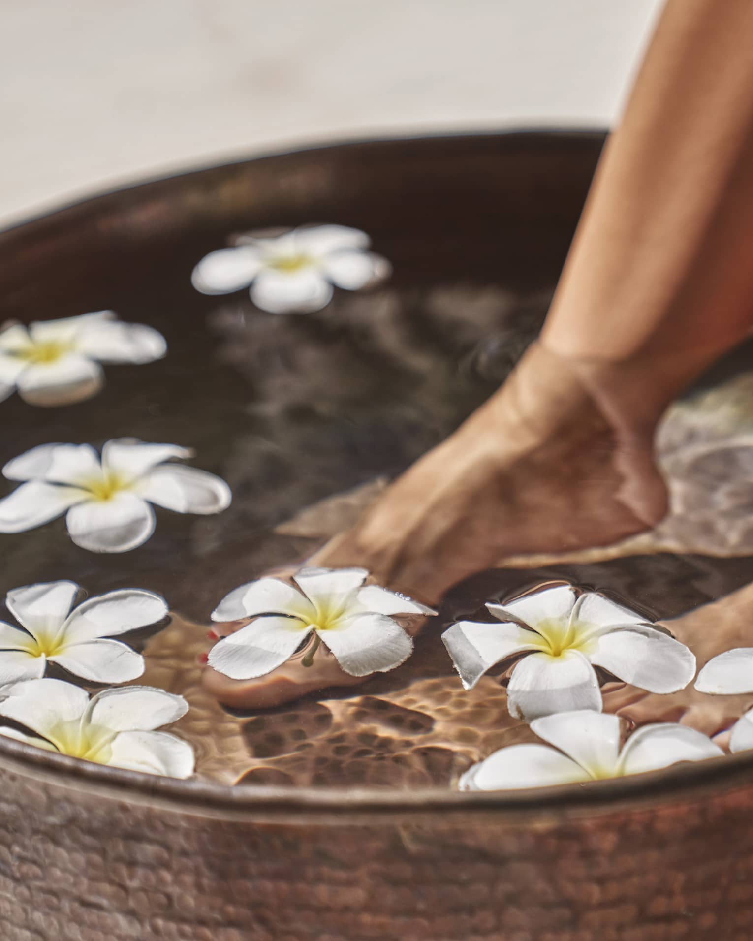 A woman's feet in a bowl of water and flowers.