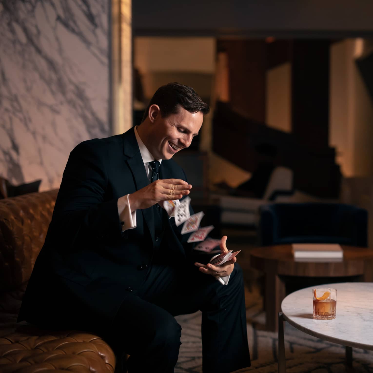 A man in a suit doing playing card drinks while sitting down.