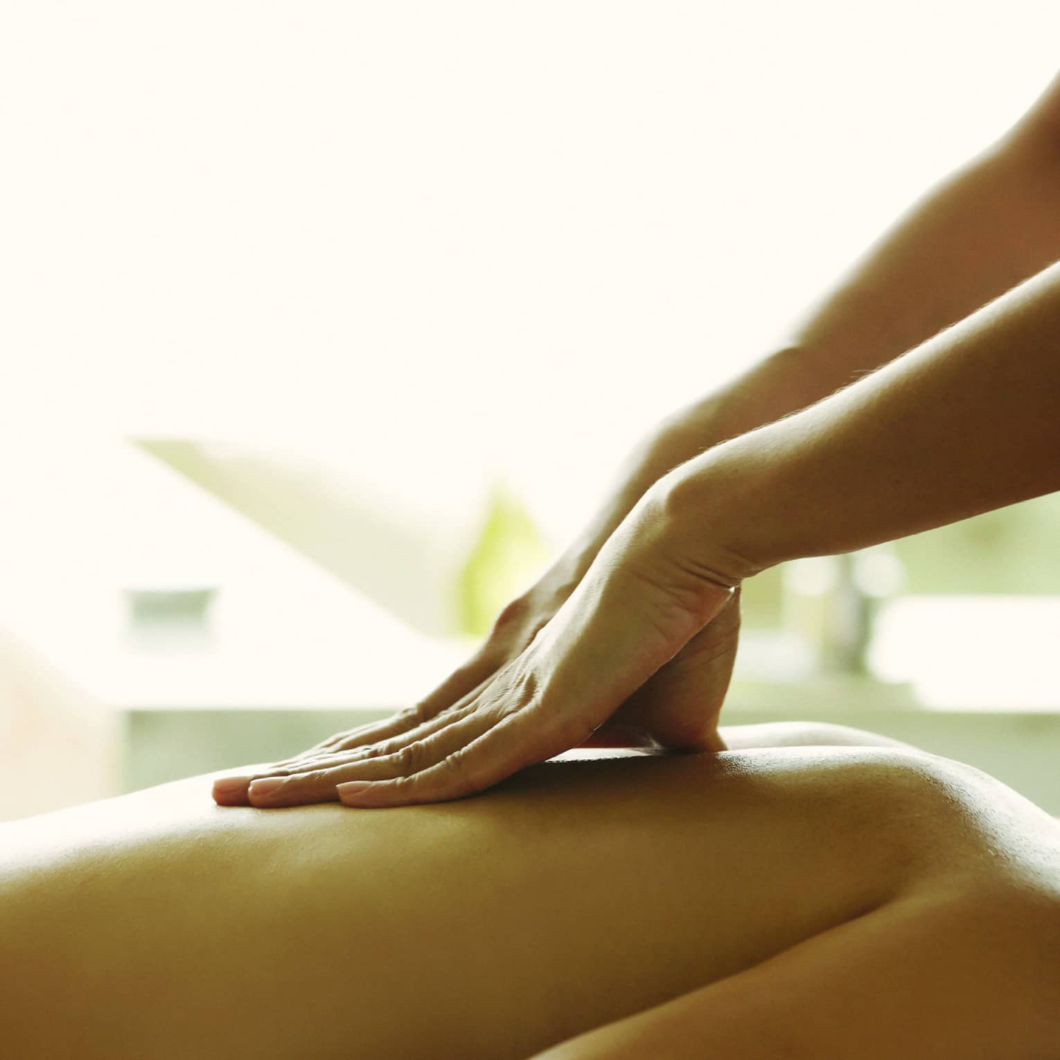 Masseuse reaches over, massages woman's bare back as she lies on spa table