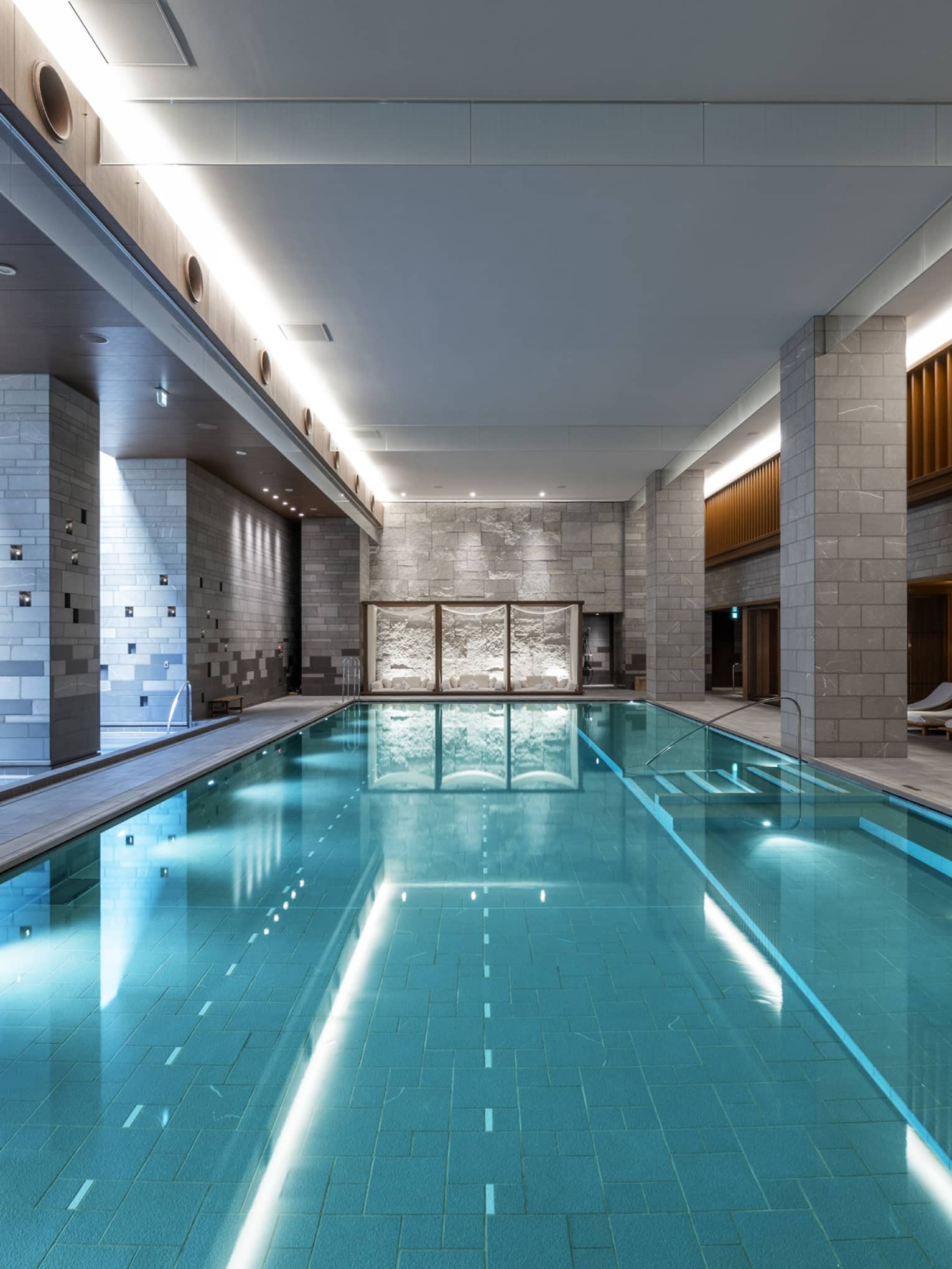Indoor spa pool flanked by chaise longues and grey brick columns