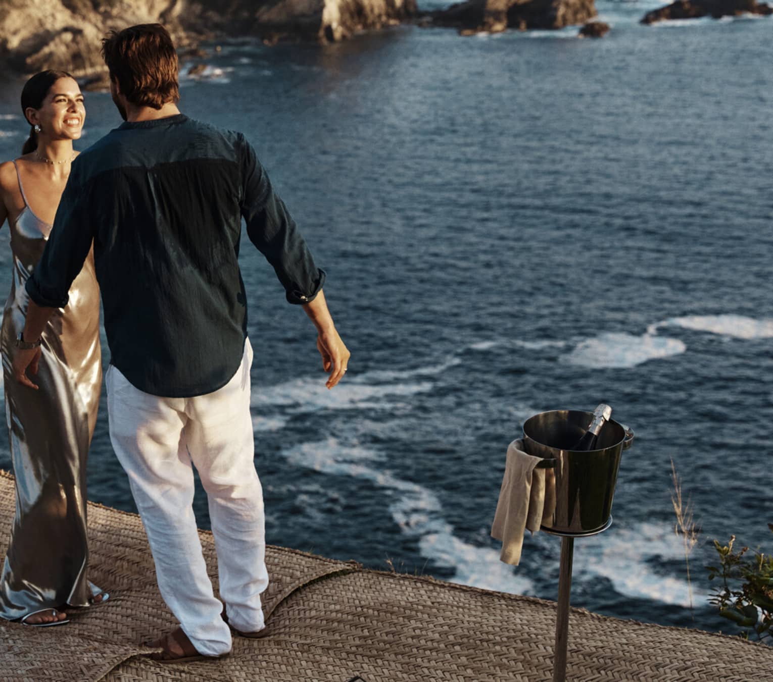 A couple standing near a vast, shimmering ocean against a backdrop of majestic cliffs, embraced by the beauty of nature