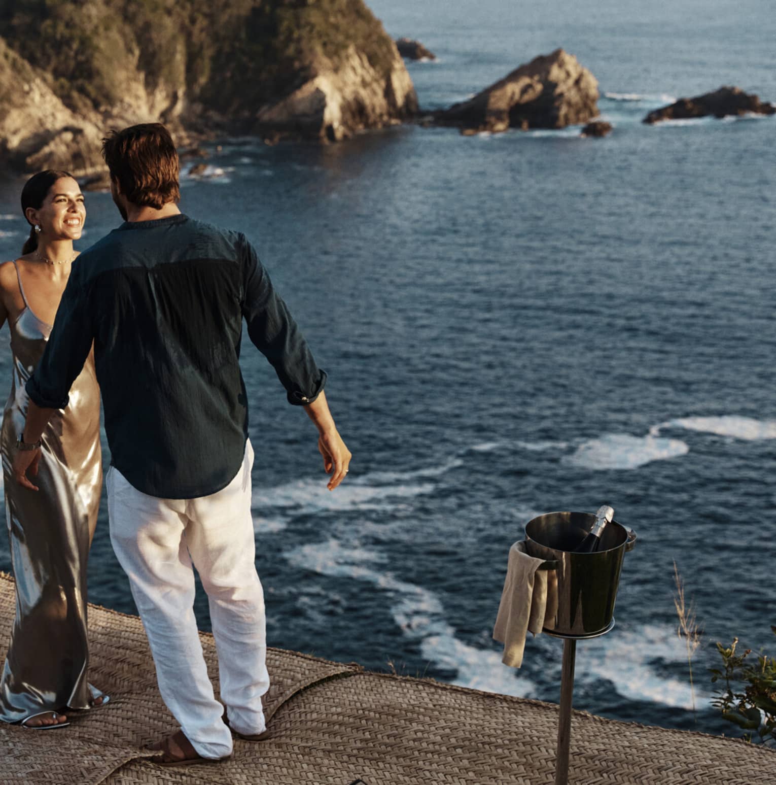 A couple standing near a vast, shimmering ocean against a backdrop of majestic cliffs, embraced by the beauty of nature