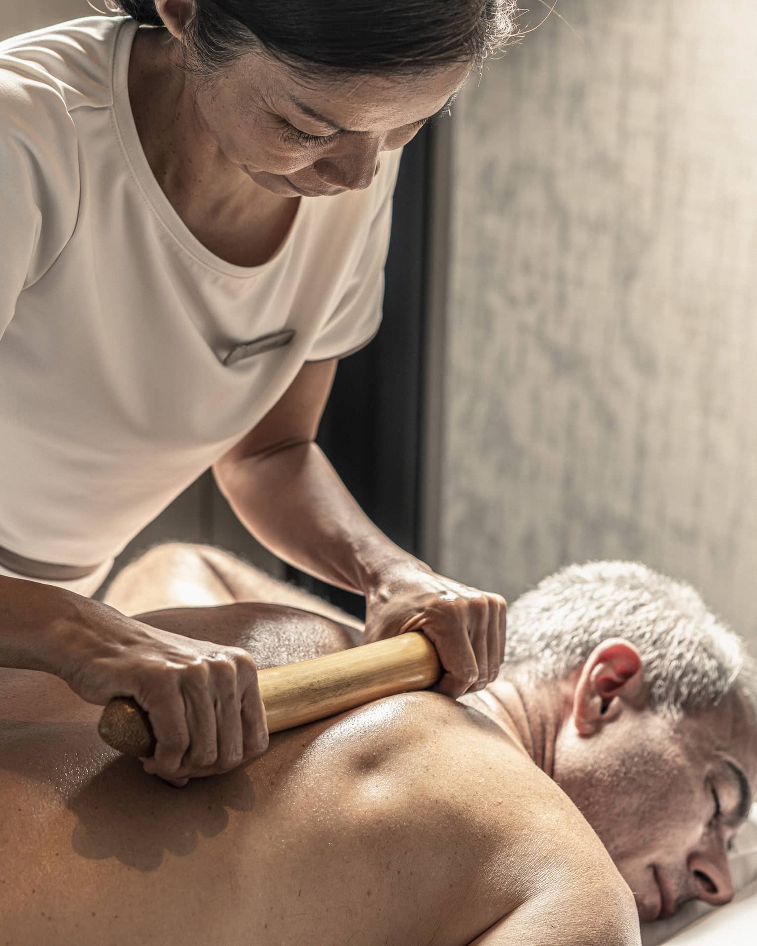 Massage therapist performs a bamboo massage on male guest