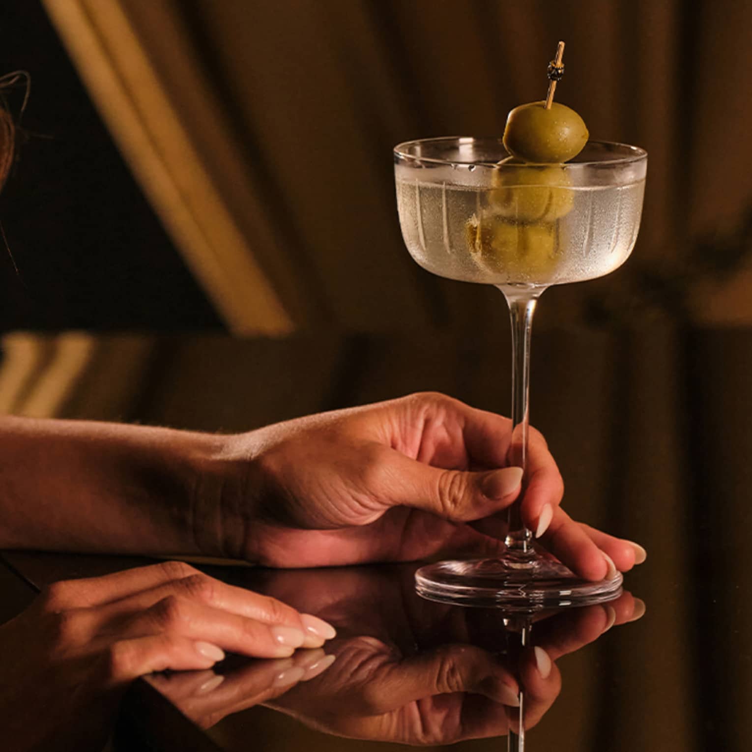 Person holding a drink glass with three olives in it.
