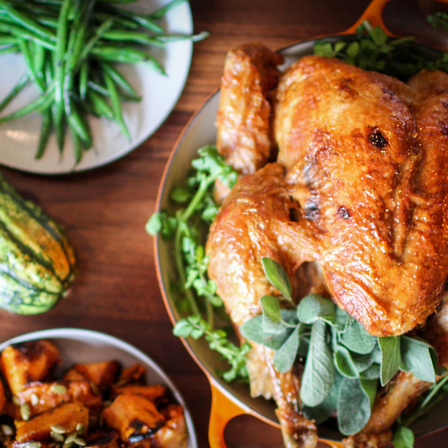 Roast turkey with fresh herbs on platter, presented on wood tabletop with gourds and green beans on white plate