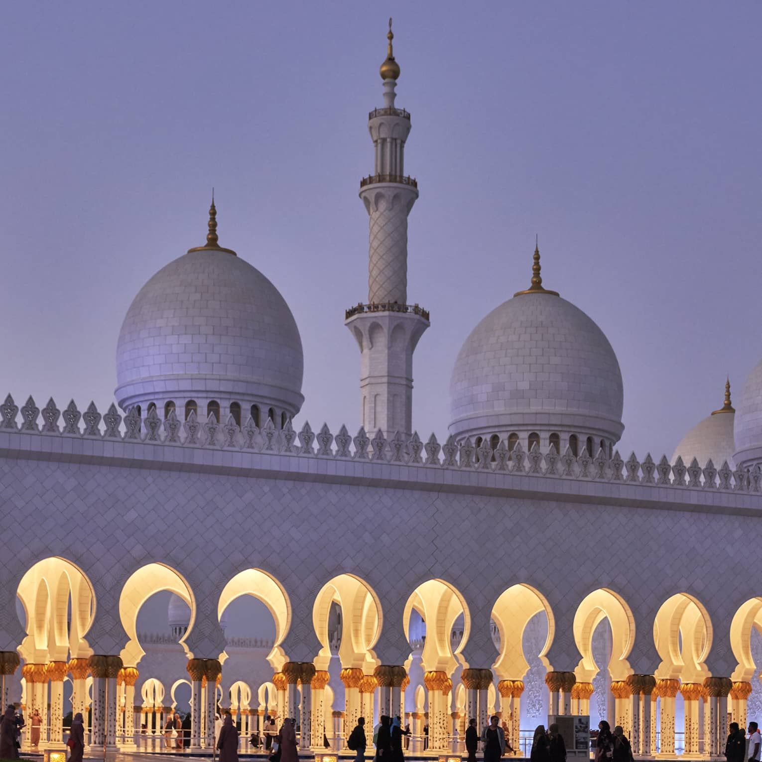 Stunning white marble mosque at dusk features a minaret with pointed domes at either side; keyhole arches line the entrance.