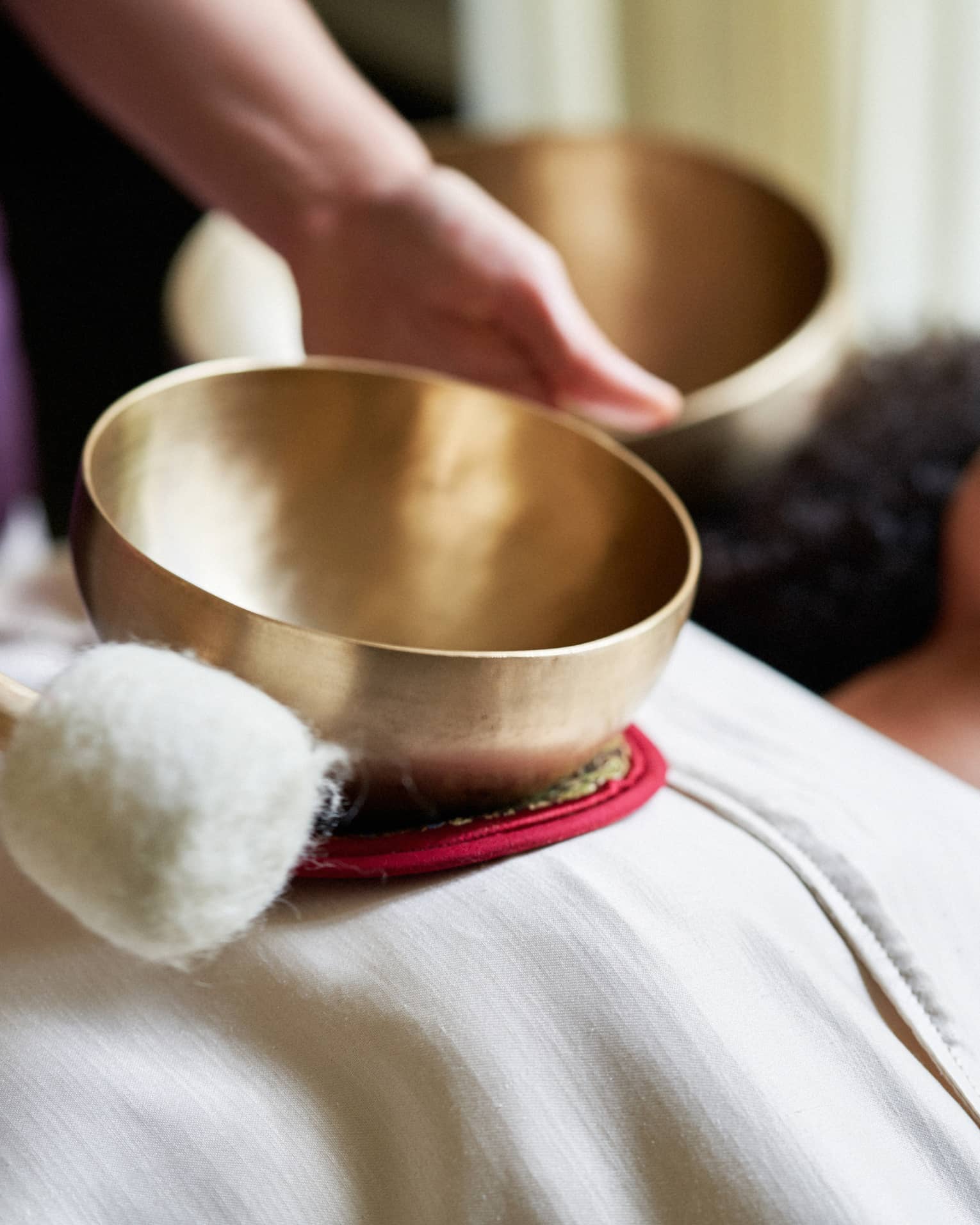 A woman with a sheet on her and a spa team member holding a golden bowl over her.