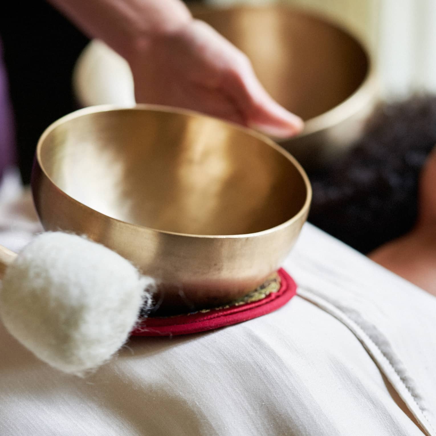 A woman with a sheet on her and a spa team member holding a golden bowl over her.
