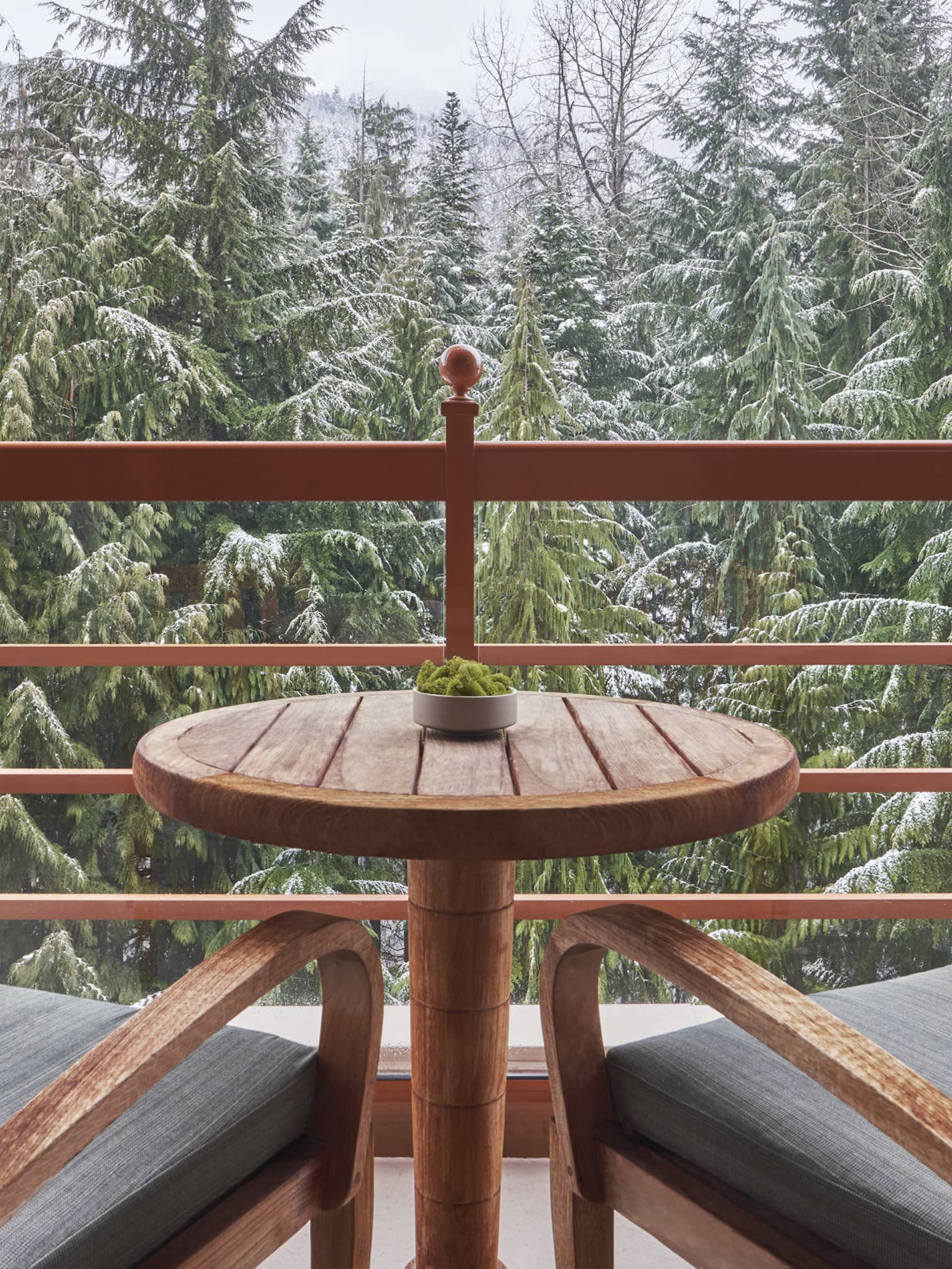 Balcony with two wooden arm chairs and a small table, overlooking the snowy forest