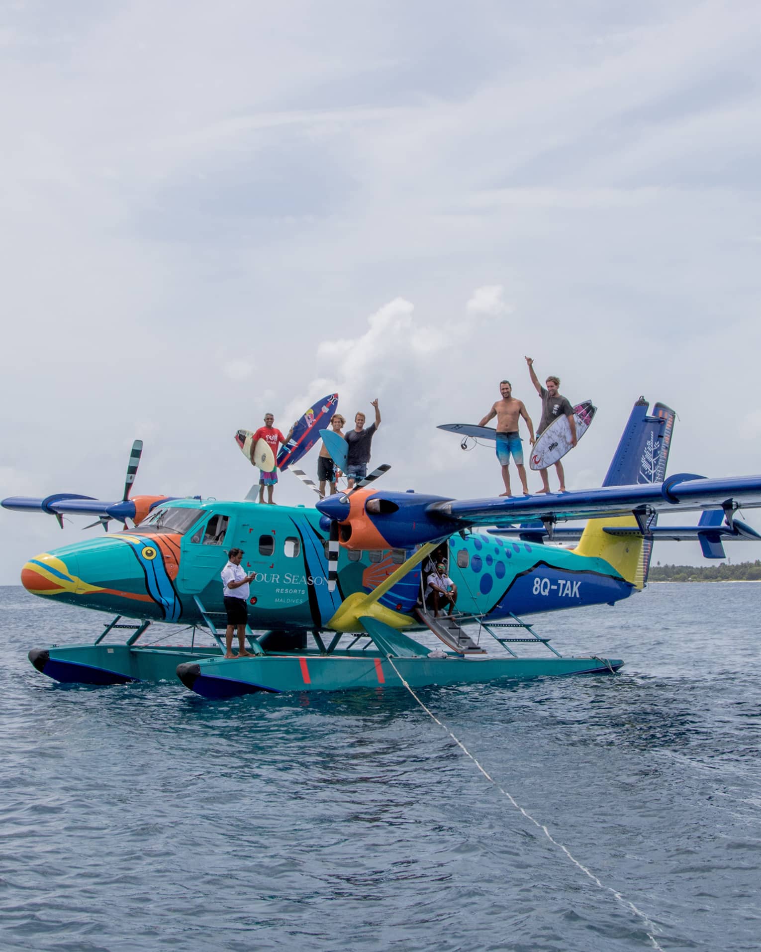 A group of people standing on top of a seaplane holding surfboards out on the water