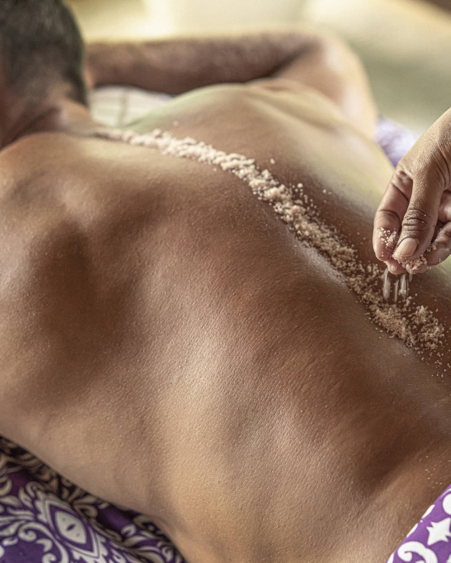 Hand place spa salts along man's spice during Sacred River Spa Massage