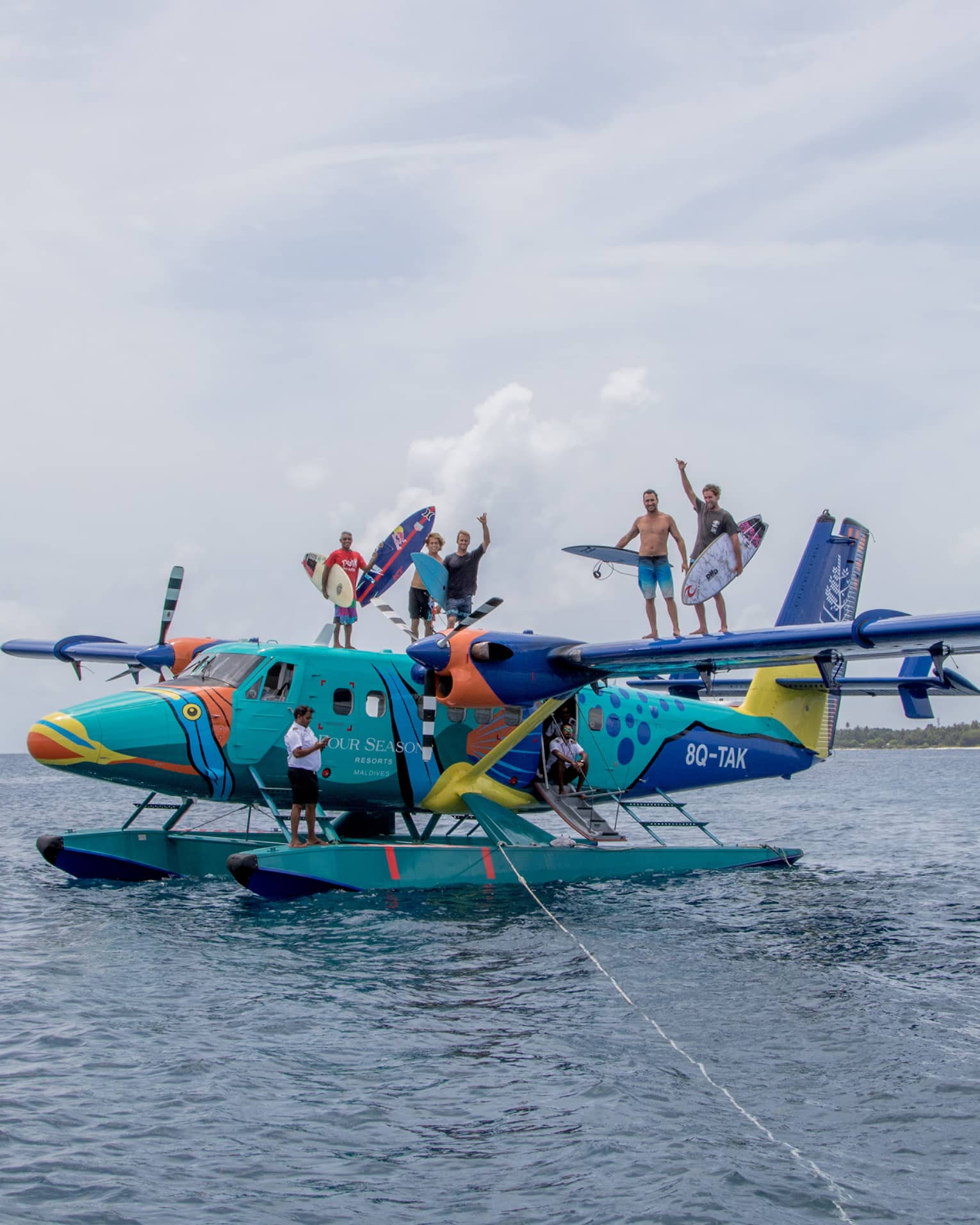 A group of people standing on top of a seaplane holding surfboards out on the water