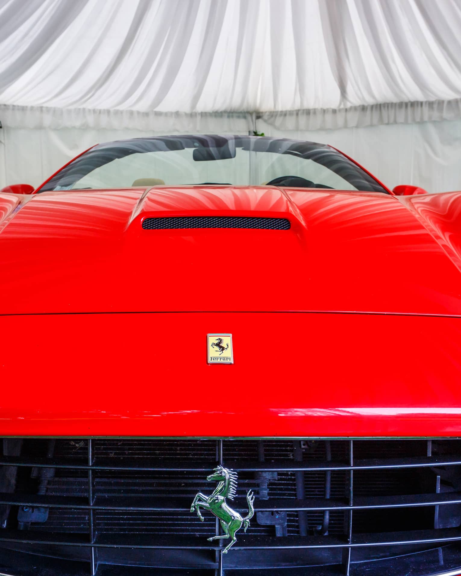 Close-up front view of a bright red Ferrari, yellow prancing horse logo on the hood and prancing horse badge on the grille.