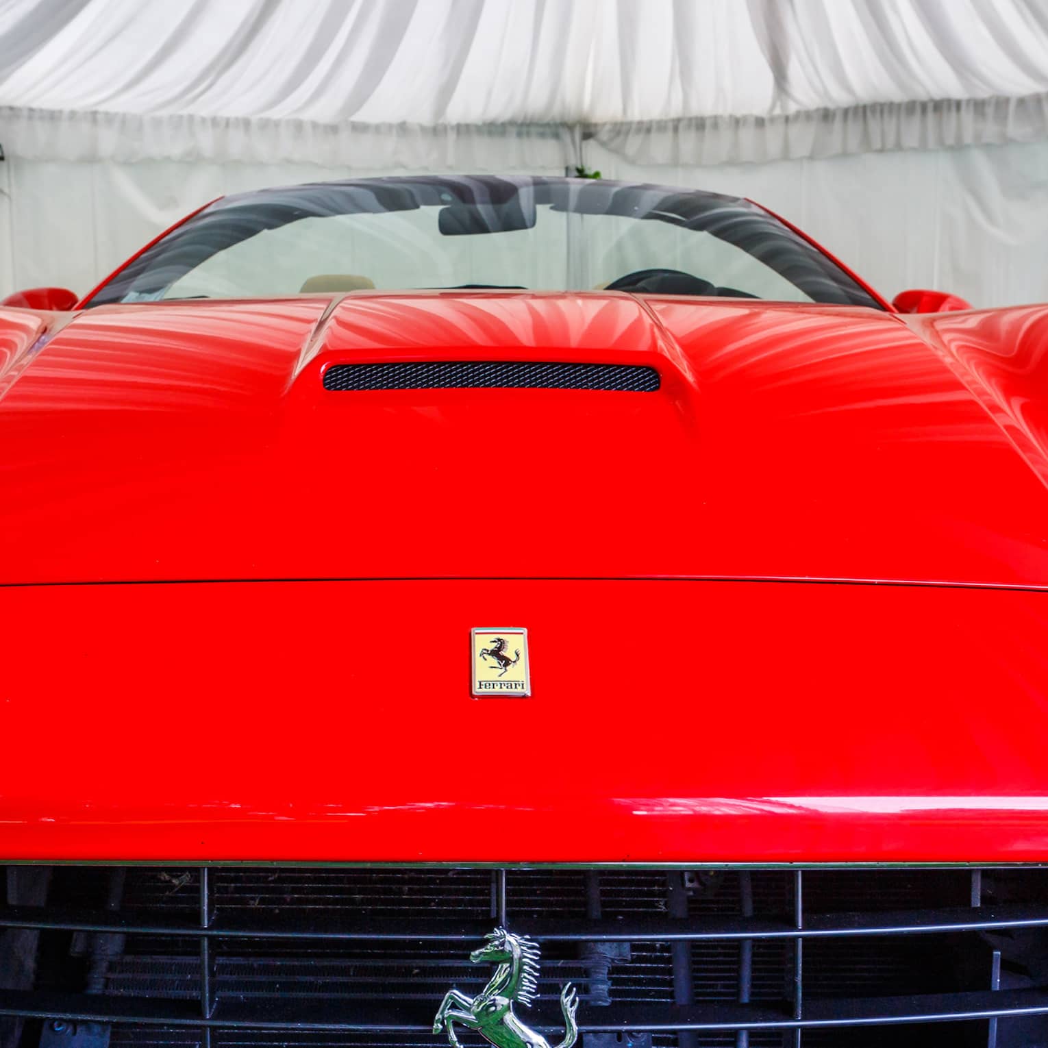 Close-up front view of a bright red Ferrari, yellow prancing horse logo on the hood and prancing horse badge on the grille.