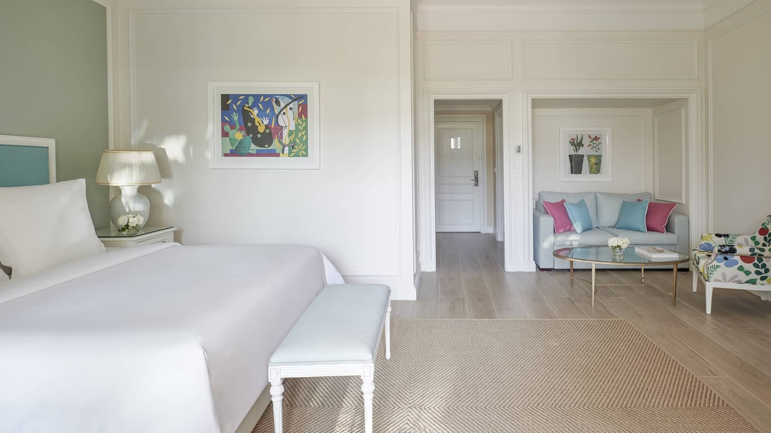 White room, white bed with blue headboard on green wall, foot bench, wood floor, seating area