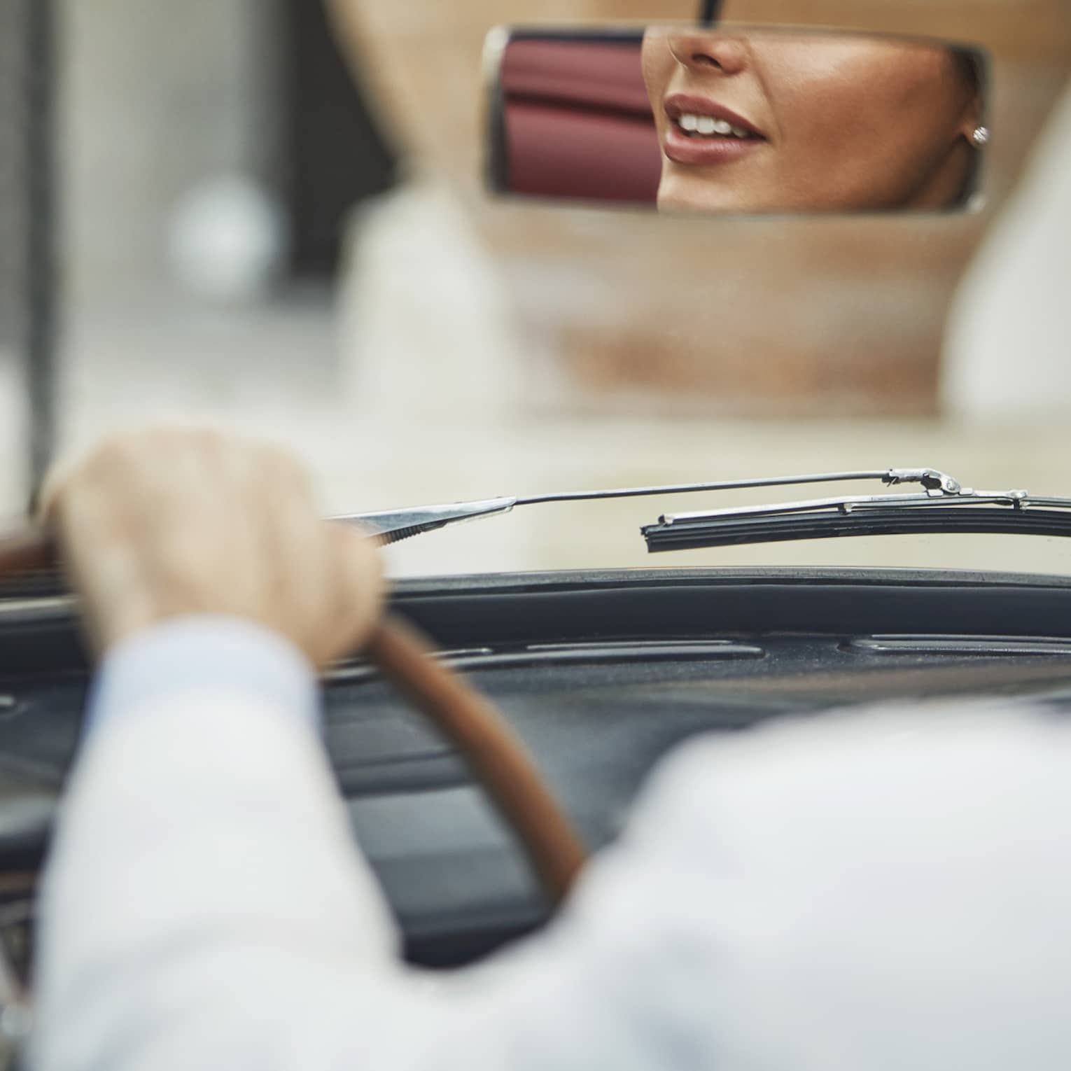 Person driving a convertible car with the reflection of another person in the rear-view mirror.