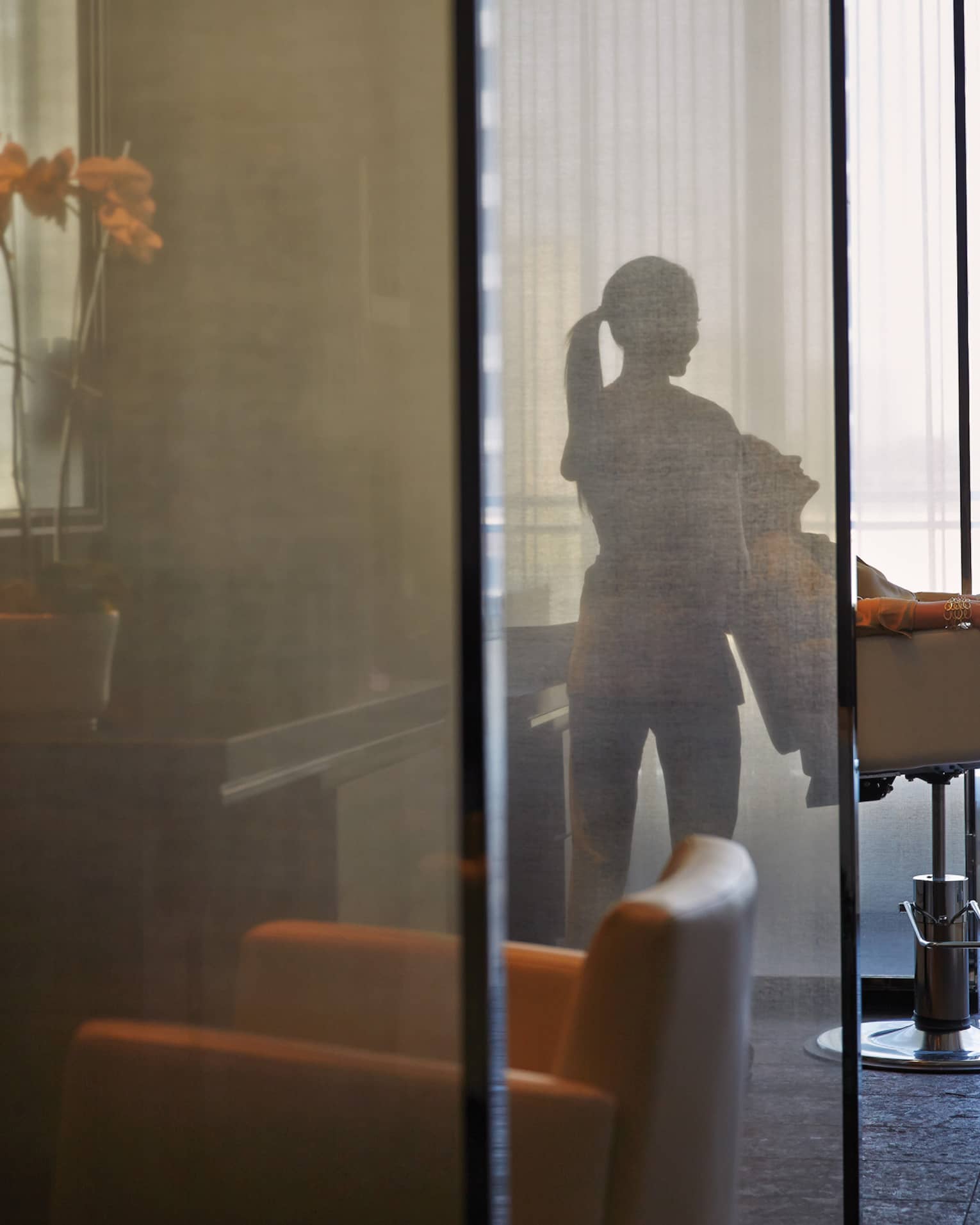 Silhouette of spa staff tilting woman back in salon chair behind sheer screen