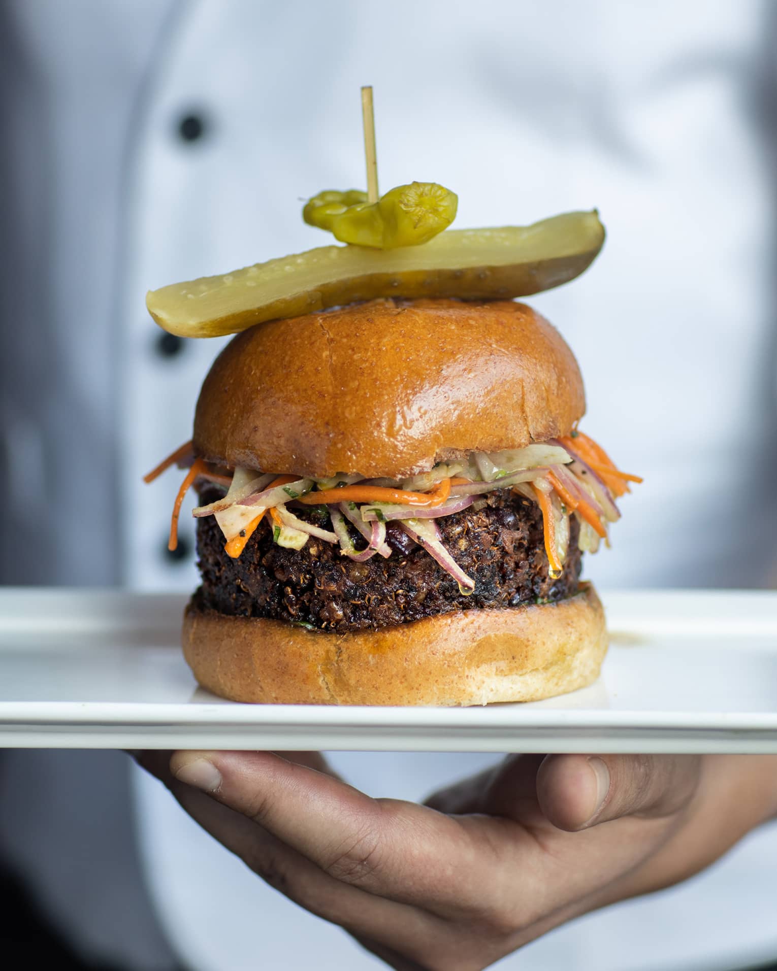 A chef holding a burger on a white plate.
