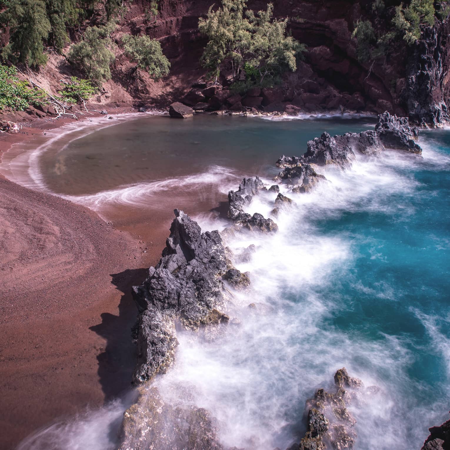 A red sand beach with waves crashing onto the sand.