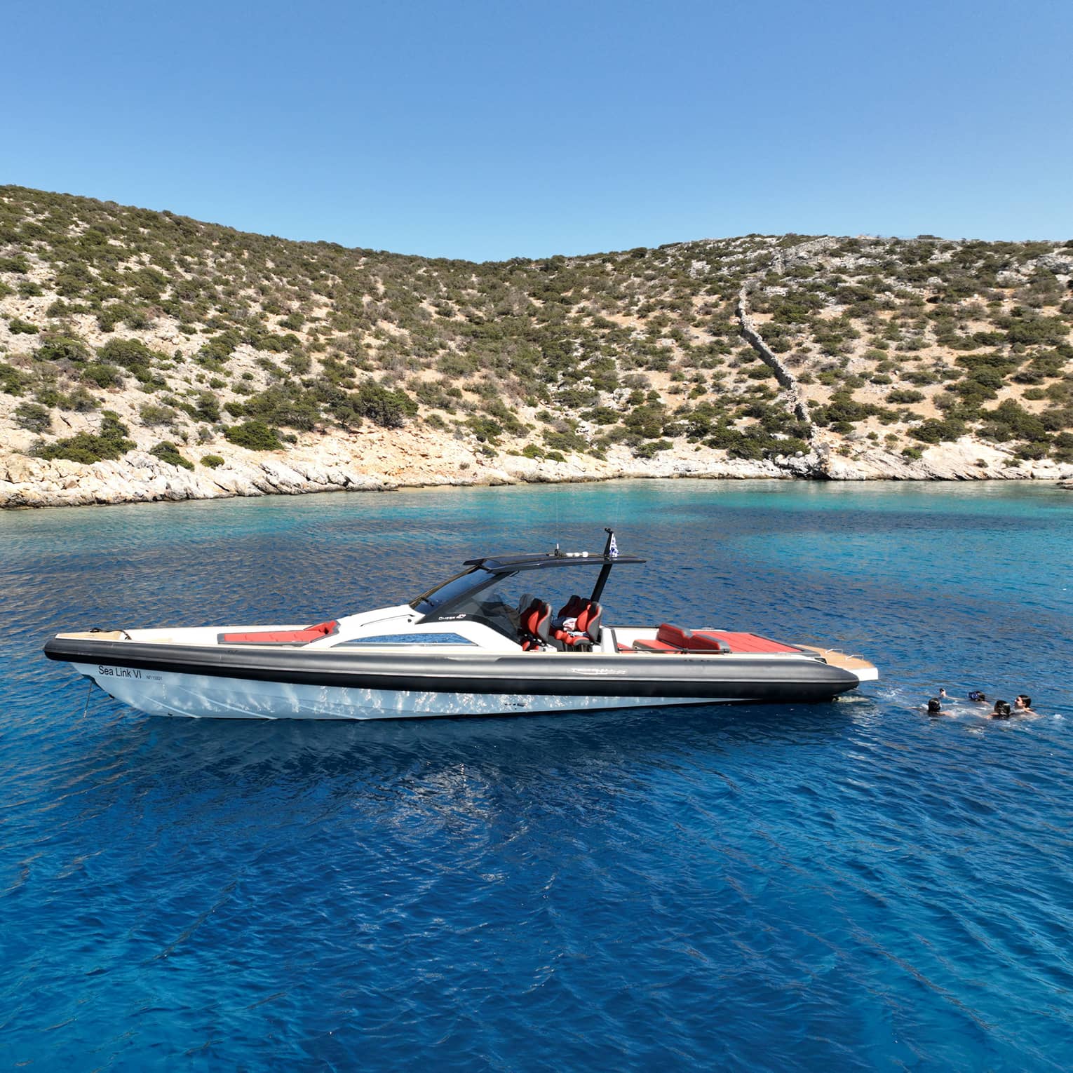 People swim behind a luxury boat in the blue waters close to the coast.