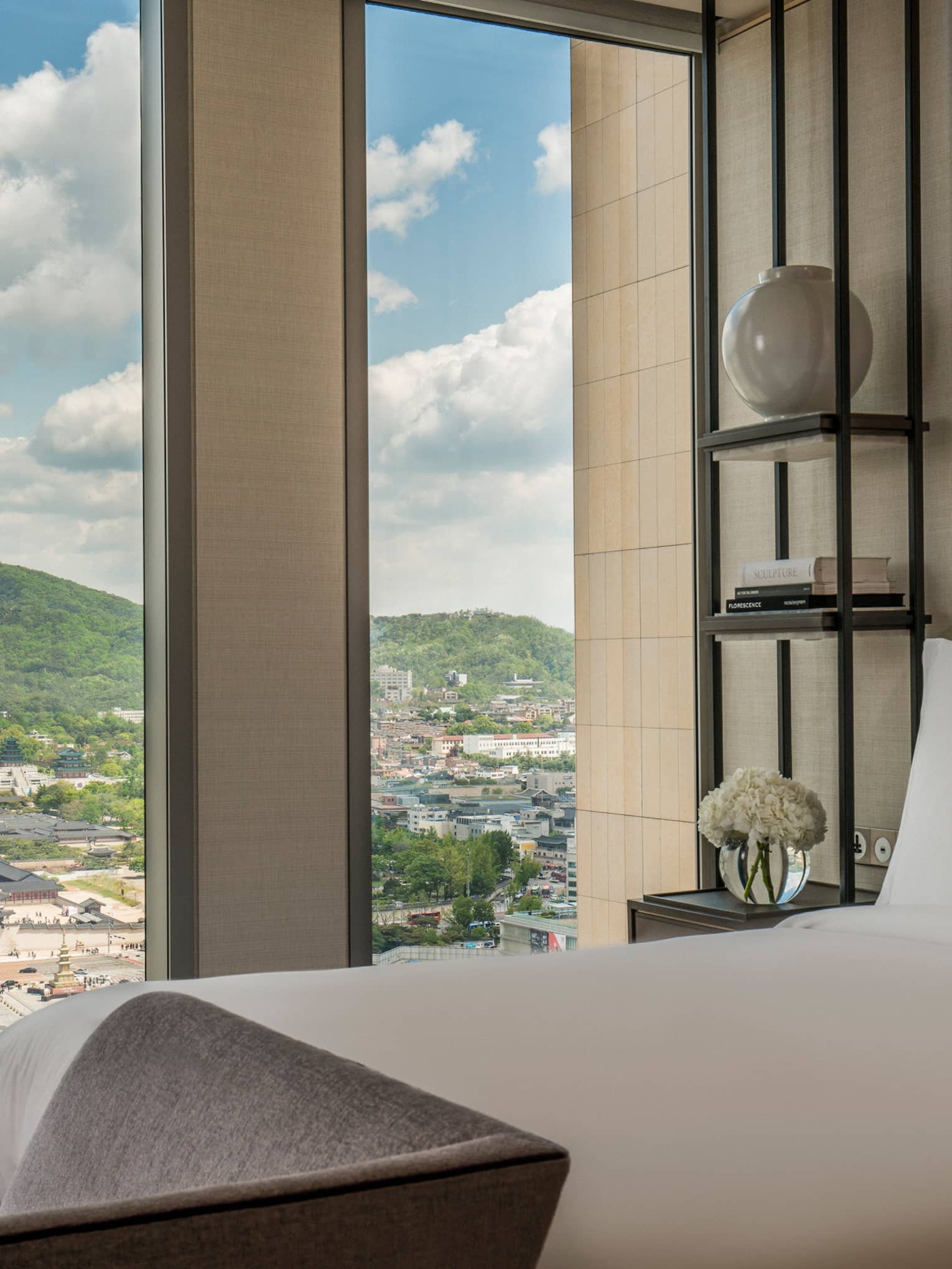 Palace-View Executive Suite bed, chaise at foot, shelf with vases, books beside window overlooking Gyeongbokgung Palace