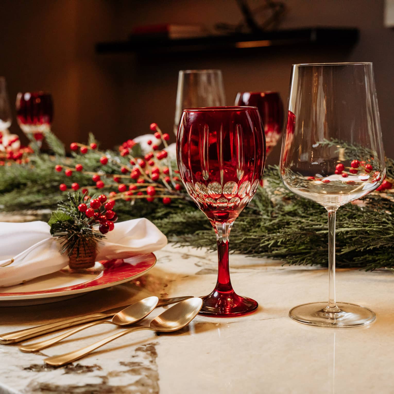 Holiday table setting with red glassware, garland and holly