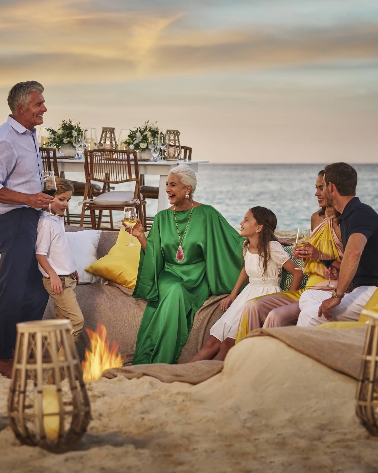 People enjoying a sunset gathering around a beach fire pit, with cozy seating and ocean view