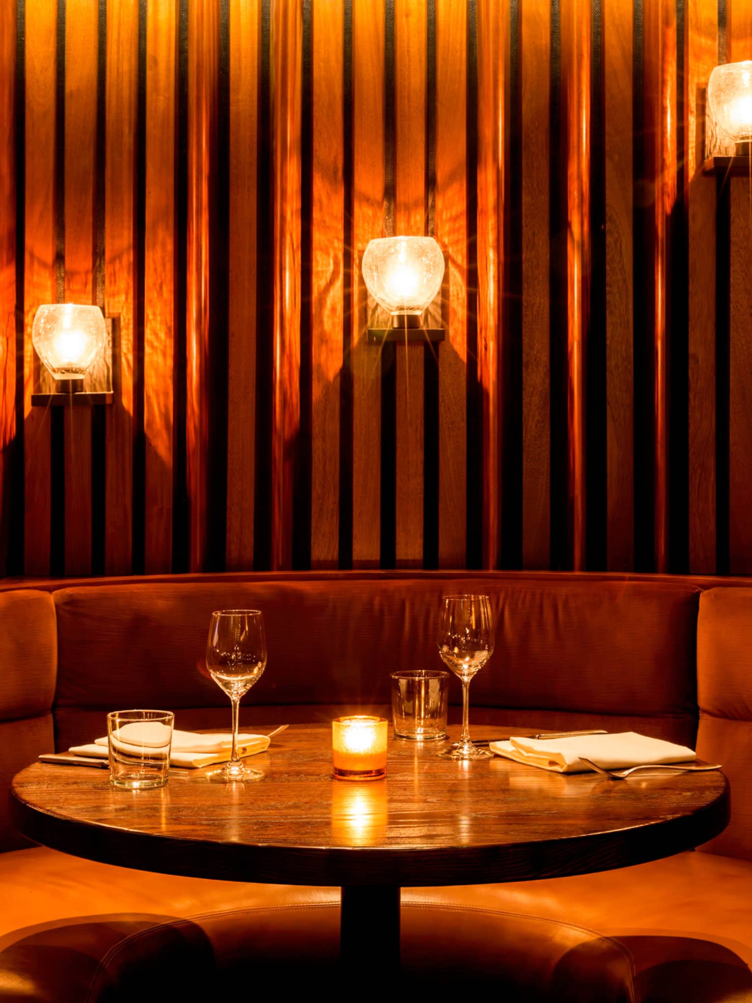 Curved plush banquette with candles, warm lights on panel wall
