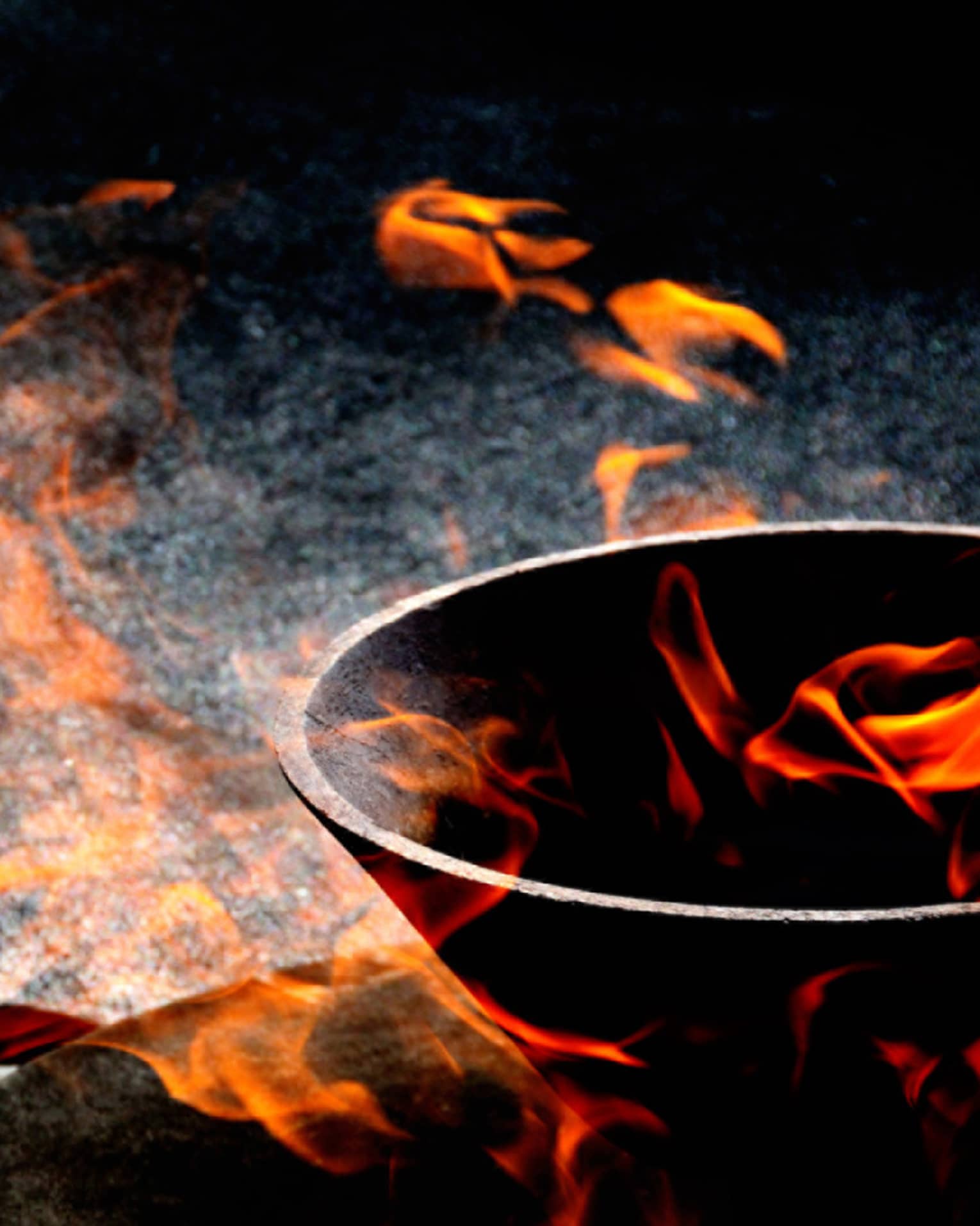Close-up view of orange-red flames appearing to float in and around a stone bowl set against a variegated dark background.