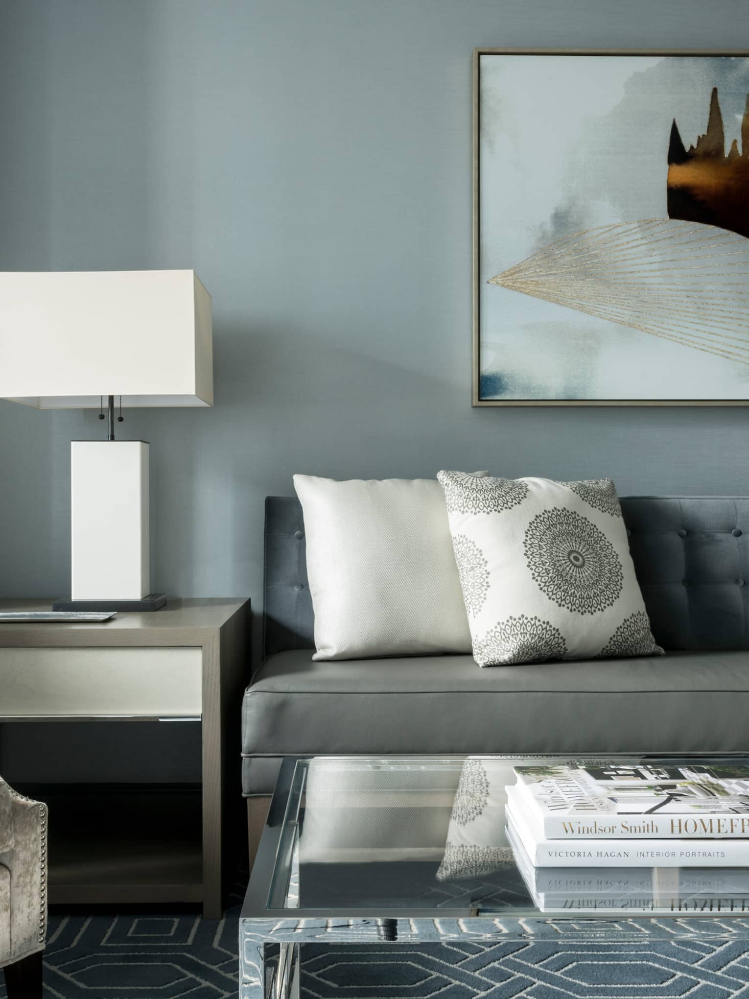 Midtown Suite long grey sofa with white accent pillows below abstract painting, table, lamp, armchair