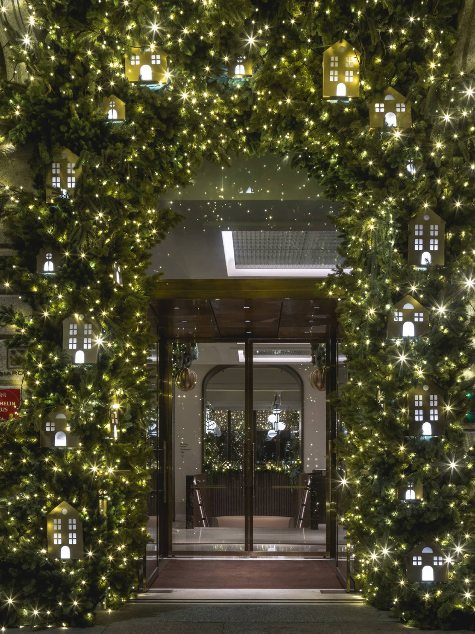 A door to a building, framed by festive greenery and holiday lights