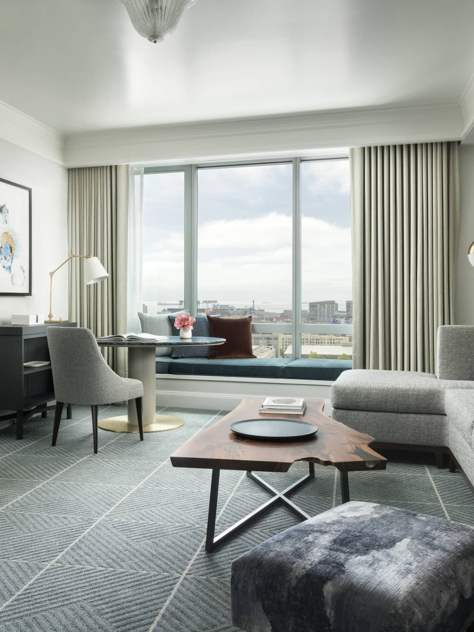 Hotel suite separate living room with retro-style L-shaped grey sofa and desk chair, live-edge wood coffee table
