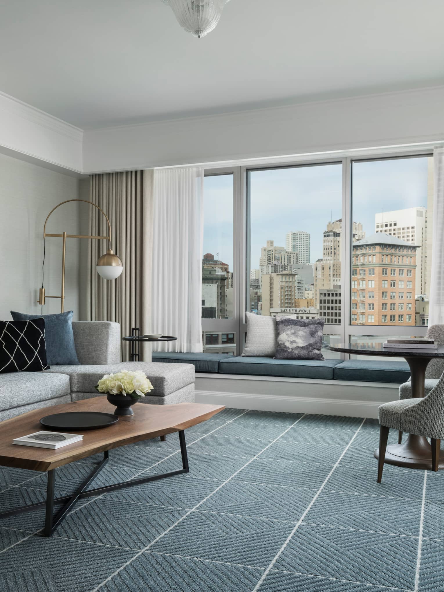 Hotel room with modern seating area, grey sofa by large window with padded bench