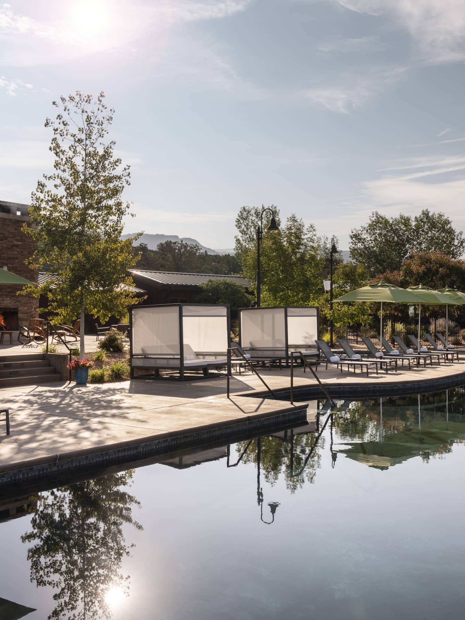 An outdoor pool with lounge chairs and green umbrellas near it.