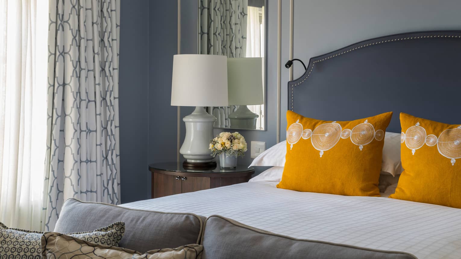 One Bedroom Suite bed with bright yellow accent pillows, white lamp on nightstand in front of mirror