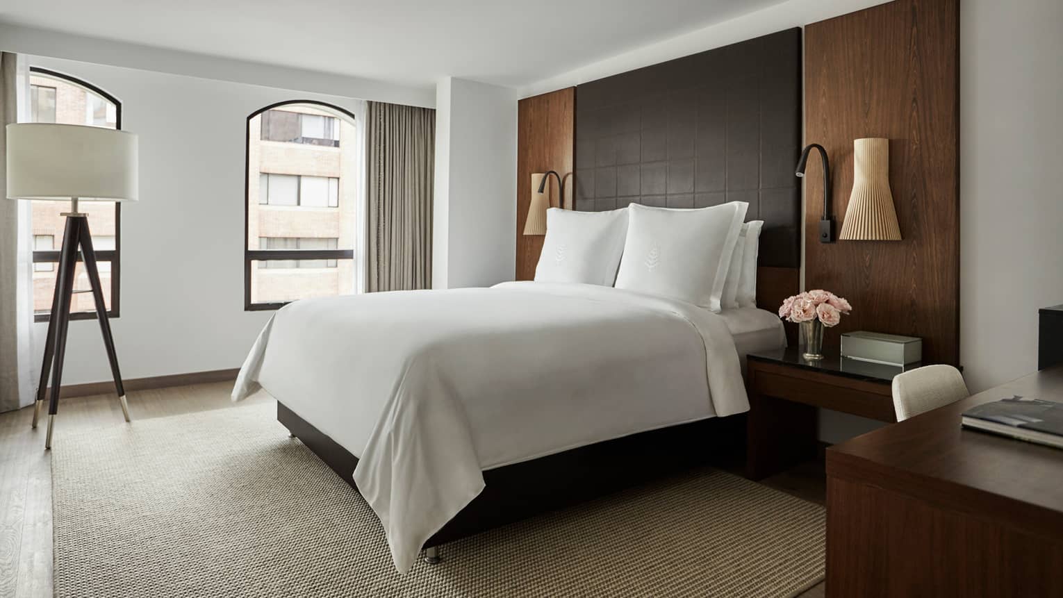 Deluxe Room bed with crisp white linens, leather and wood headboard, wood tripod lamp with white shade