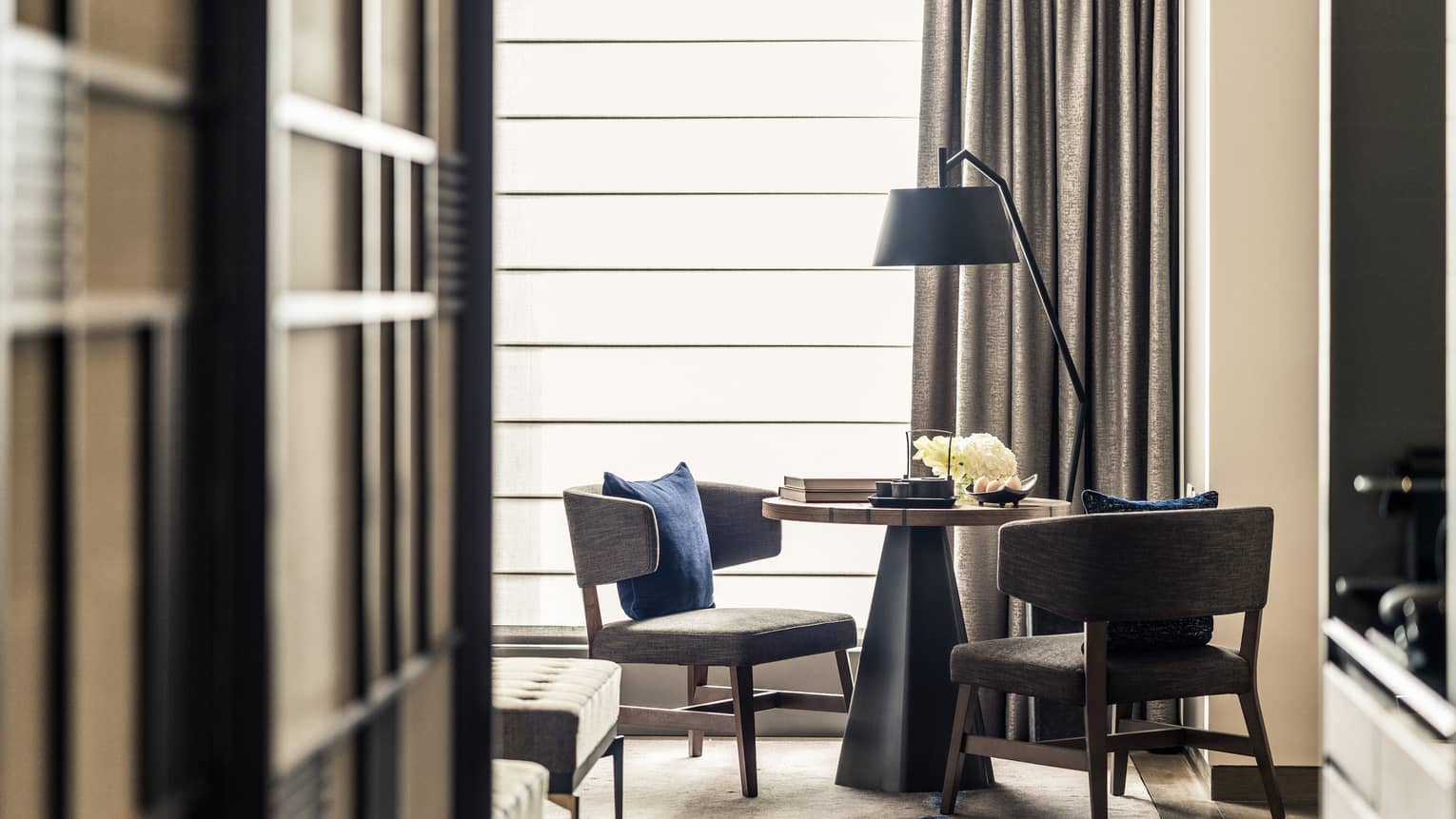 Cozy seating area with two chairs, a round table and a floor lamp, set near a large window 