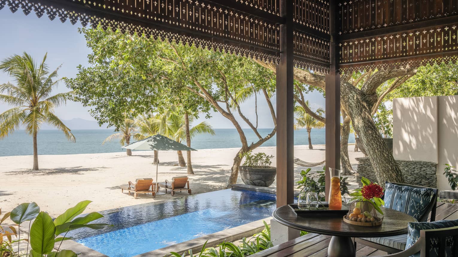 View of pool, beach and sea from covered terrace lounge