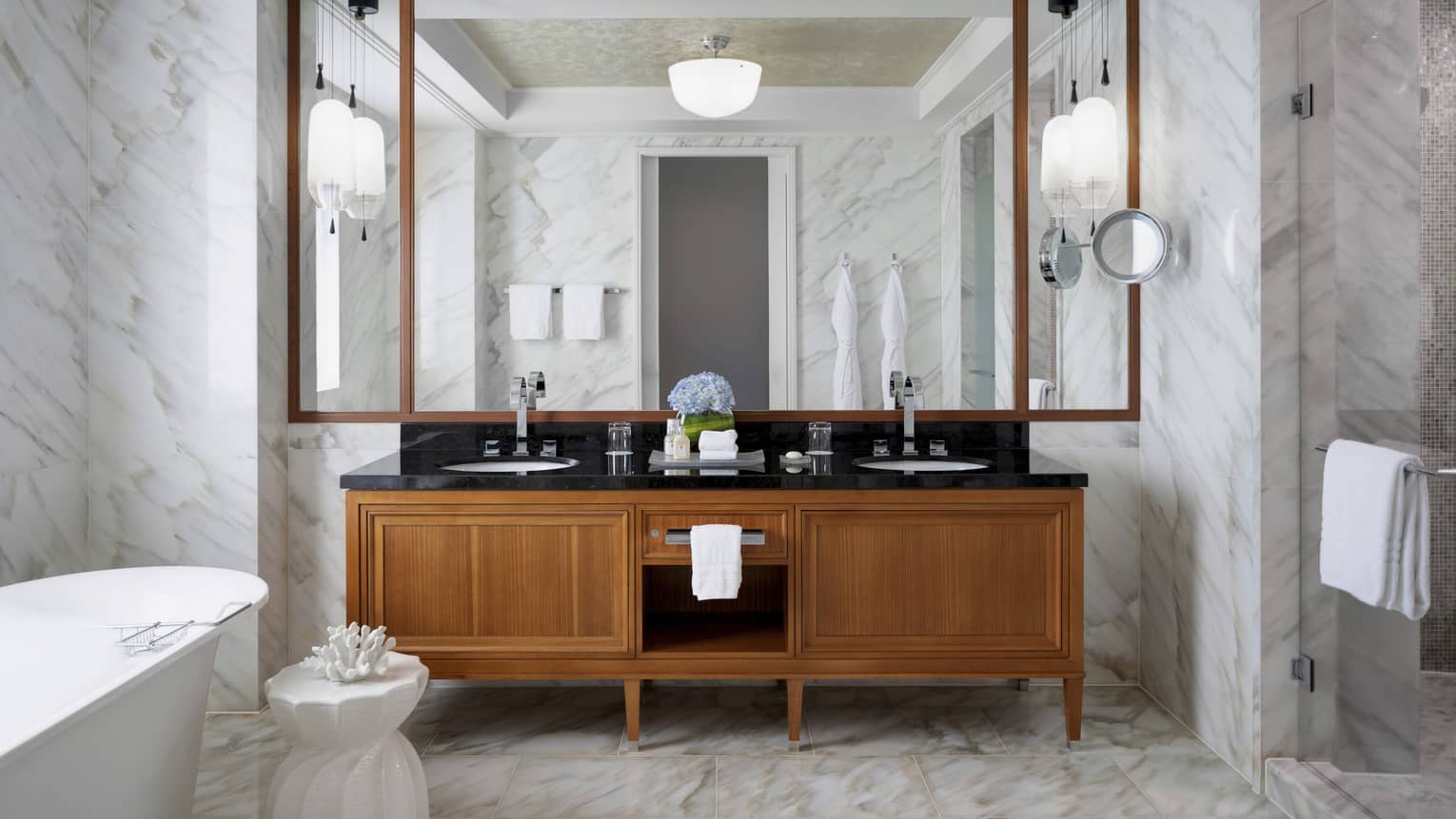 Large bathroom with marble floors and walls, wooden vanity and freestanding tub