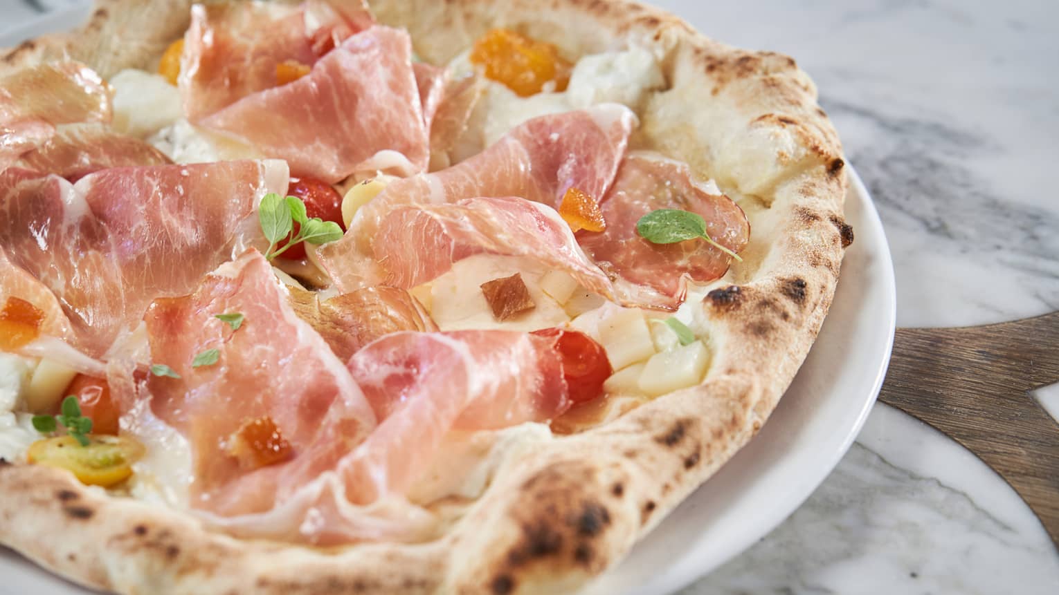 A signature pizza with prosciutto, cherry tomatoes and apricot 