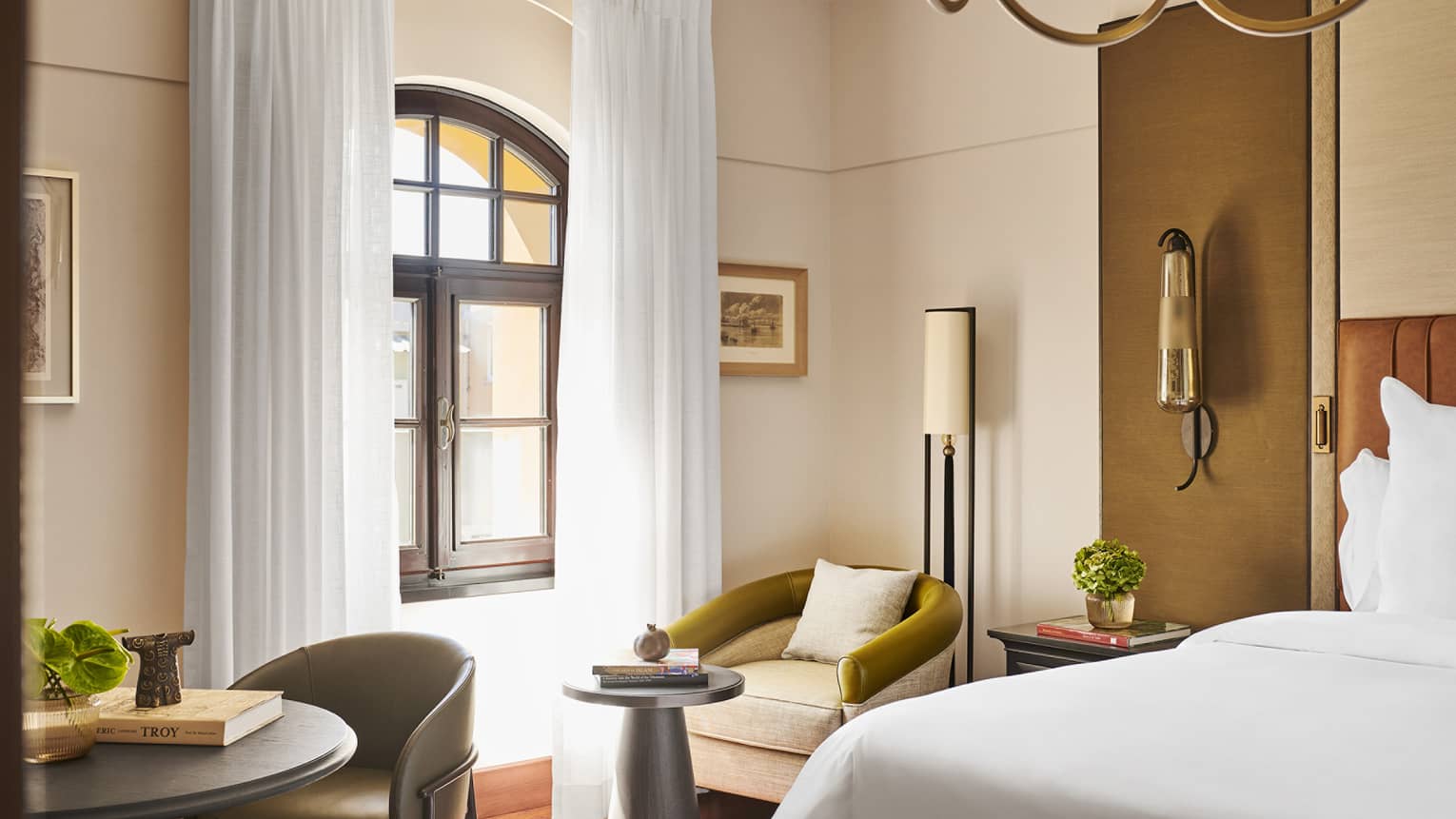 Bedroom with king bed, armchair, arched window, round table with chair