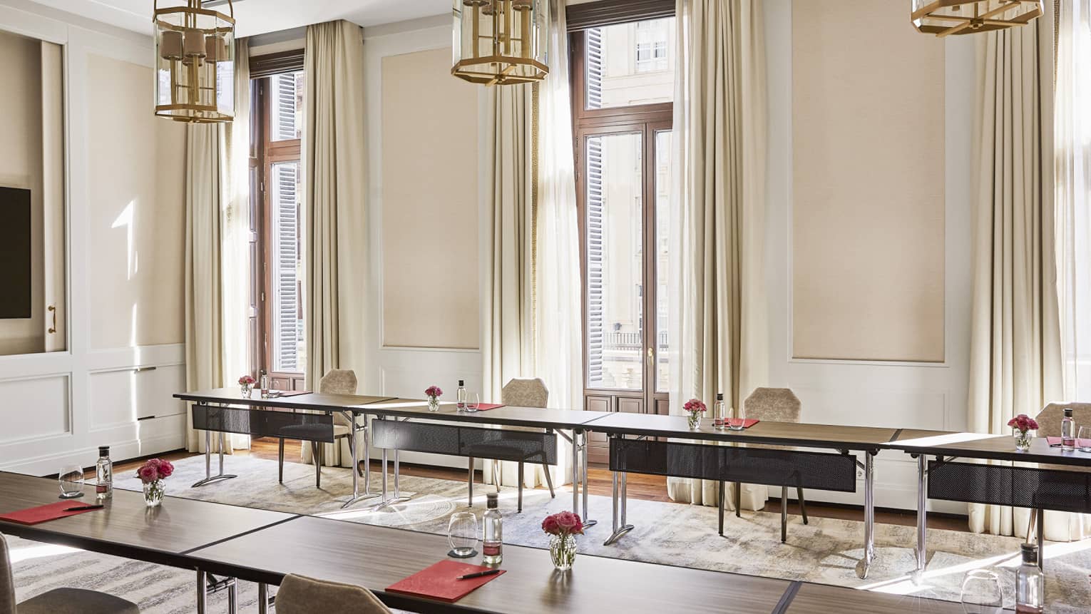 Meeting room with u-shape table set-up, three small chandeliers hanging from ceiling, three windows