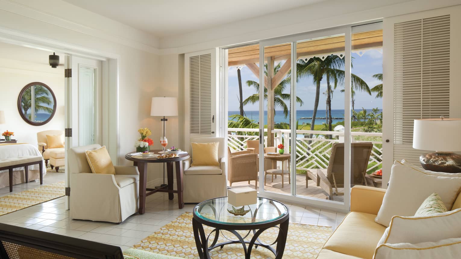 Bright Plantation Suite living room, white sofas, small glass table, balcony doors with shutters
