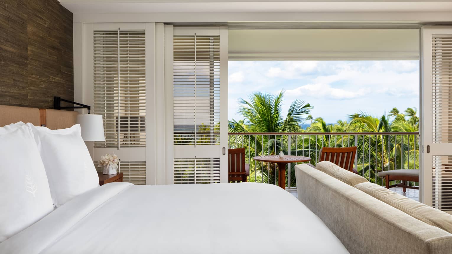 Hotel room with king bed and balcony overlooking palm trees