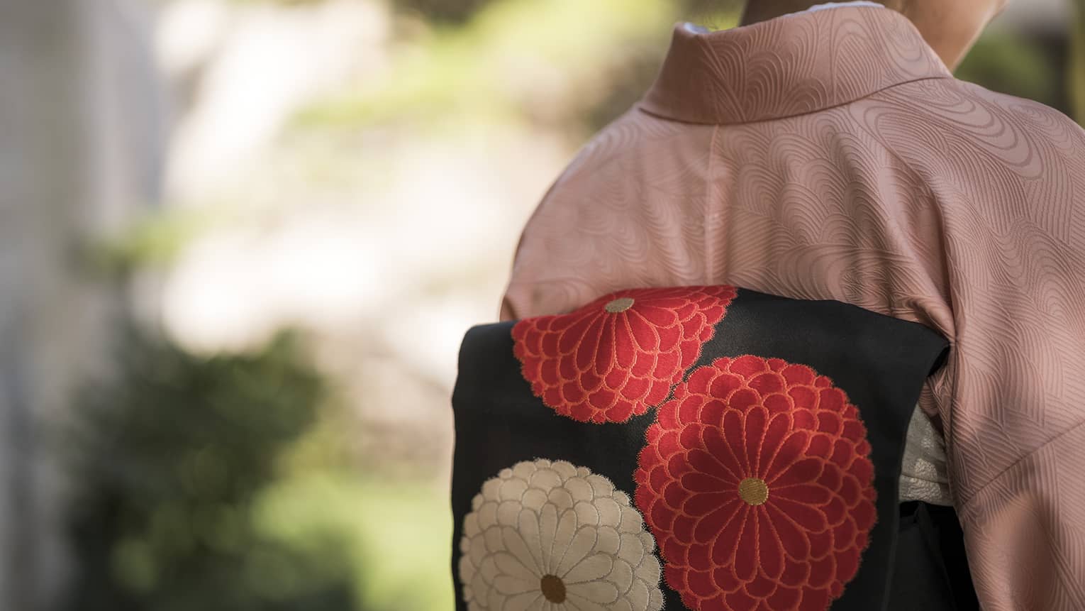 Back view of a person wearing a pink kimono with a black obi featuring red and white floral designs