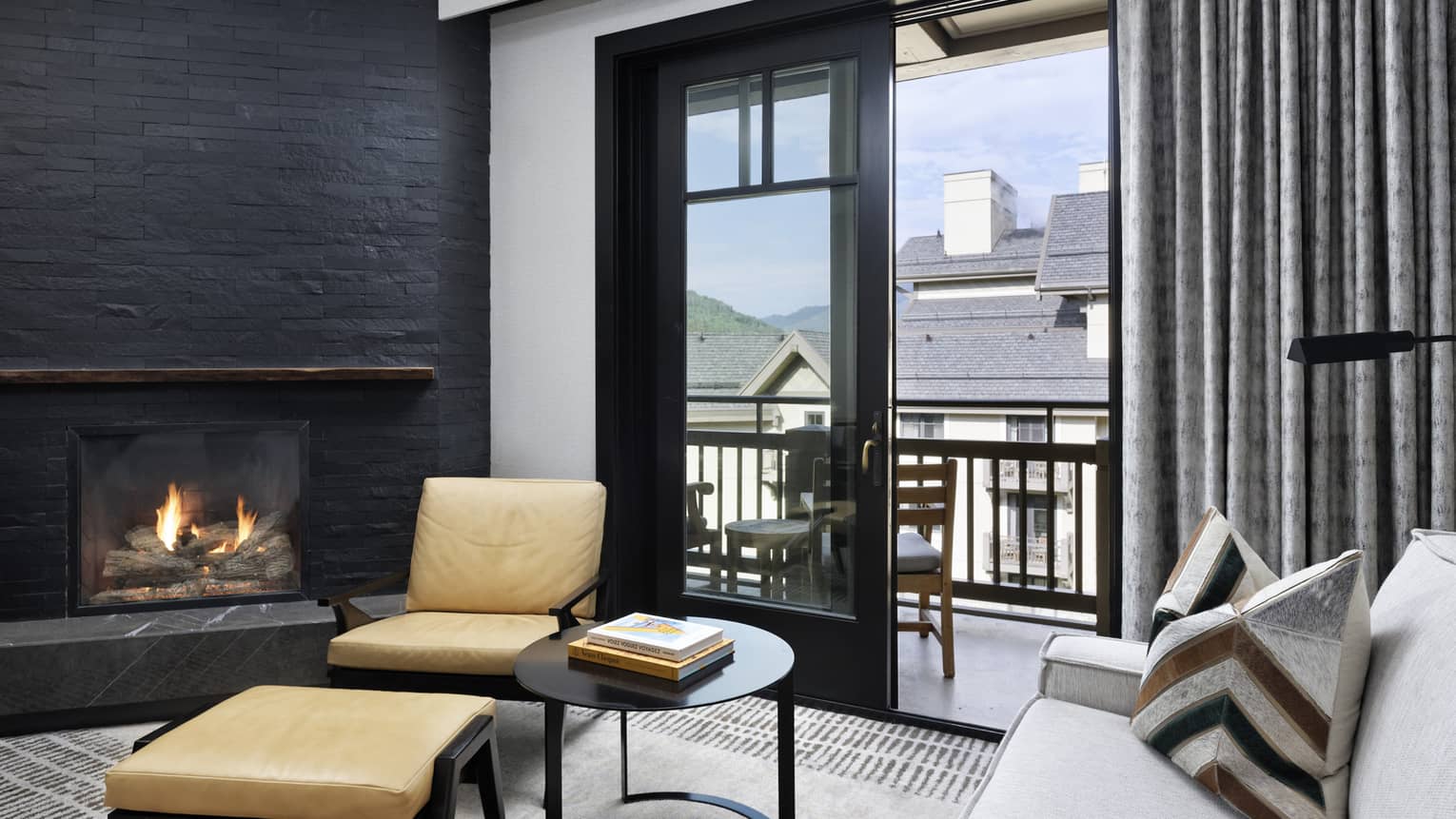 White sofa, corner stone fireplace, arm chair and ottoman, sliding glass door leading to balcony