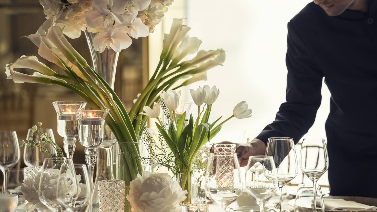 Hotel staff sets elegant banquet dining table with crystal glasses, vases with white flowers