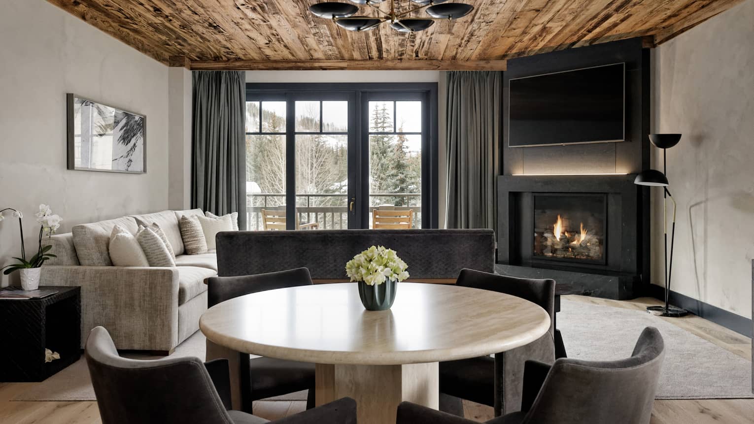 Round dining table with four chairs in a living room with fireplace and wooden ceiling