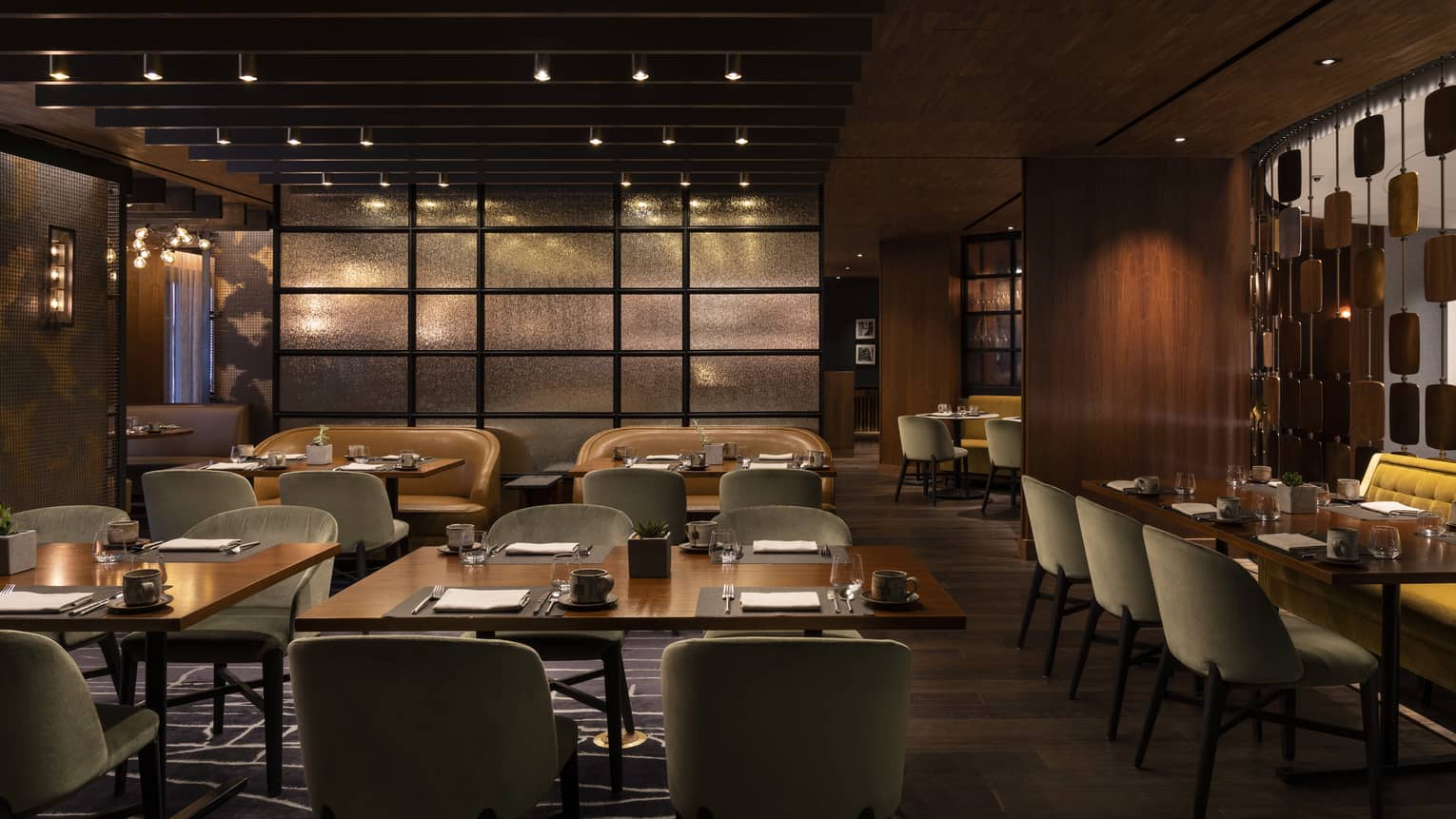 The interior of a dimly lit restaurant with square tables, grey chairs and wood walls.